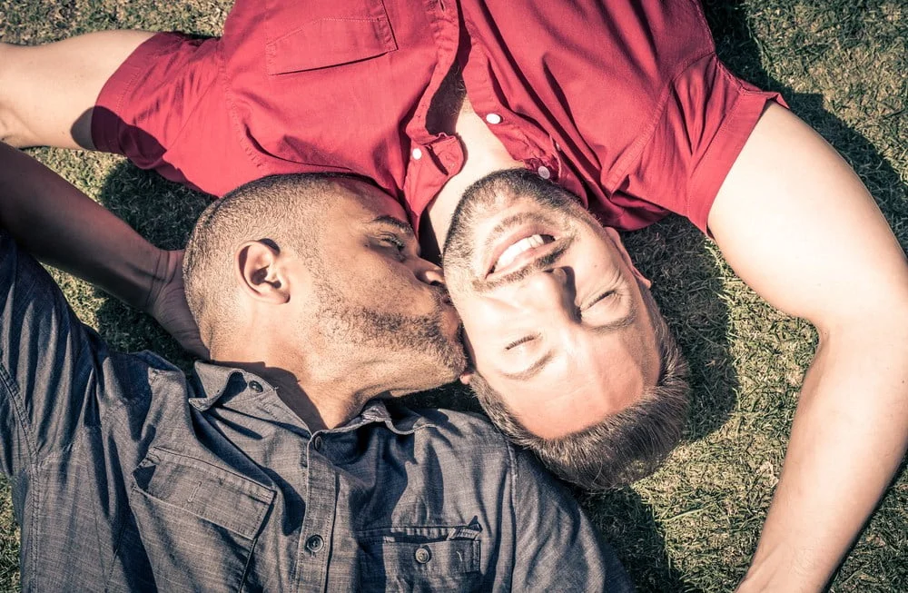 Dois homens deitados na relva, um com uma camisola vermelha a beijar a testa do outro com uma camisola cinzenta, desafiando de forma bela alguns dos maiores mitos sobre a homossexualidade.