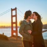 Duas pessoas com casacos compartilharam um beijo ao pôr do sol em frente à Ponte Golden Gate, capturando um momento perfeito que certamente receberá muitos gostos no Facebook.