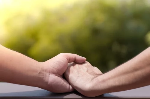 Duas mãos a segurar-se uma à outra com um fundo verde desfocado, simbolizando a união e a força para superar nossas inseguranças.