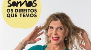 Uma mulher de cabelo comprido e batom vermelho sorri, tocando no cabelo com as duas mãos. No texto da imagem lê-se "SOMOS OS DIREITOS QUE TEMOS" em português, incorporando o espírito de resiliência face aos preconceitos em Portugal.