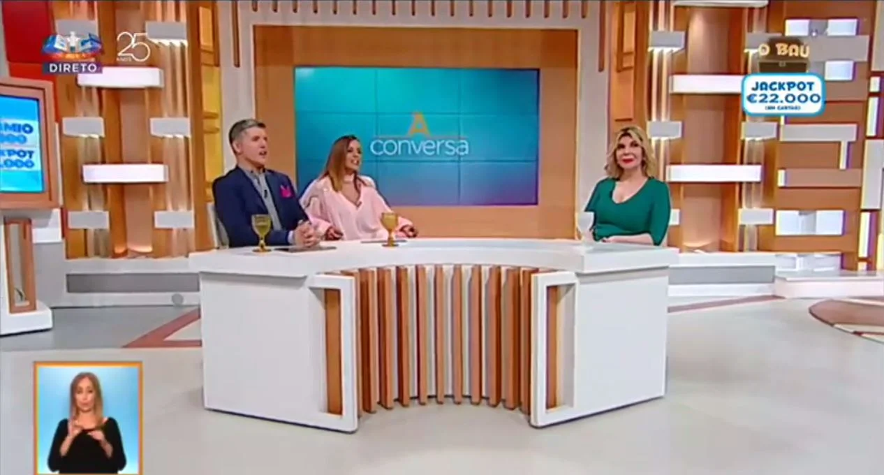 Três pessoas sentaram-se a uma secretária curva, a conversar num estúdio de televisão. No canto inferior esquerdo, é um intérprete de língua gestual e, ao fundo, vê-se a palavra "conversa", enquanto discutem temas como tabus e o que significa ser transexual.