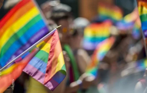 Bandeiras coloridas do orgulho LGBTQ+ são agitadas por uma multidão num desfile ou evento de celebração, em solidariedade contra a realidade de que a homossexualidade ainda é ilegal em 72 países.