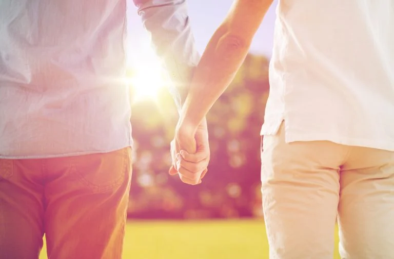 Duas pessoas dão as mãos enquanto caminham ao ar livre, com a luz do sol a brilhar por entre os seus braços, o que me faz lembrar os passeios que costumava dar com o meu pai.