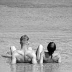 Casal nu deitado na praia de frente para o mar