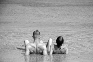 Casal nu deitado na praia de frente para o mar