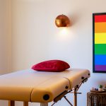 Imagem de uma sala de massagem com quadro LGBTI na parede e uma mesa de massagem pronta para receber um cliente.