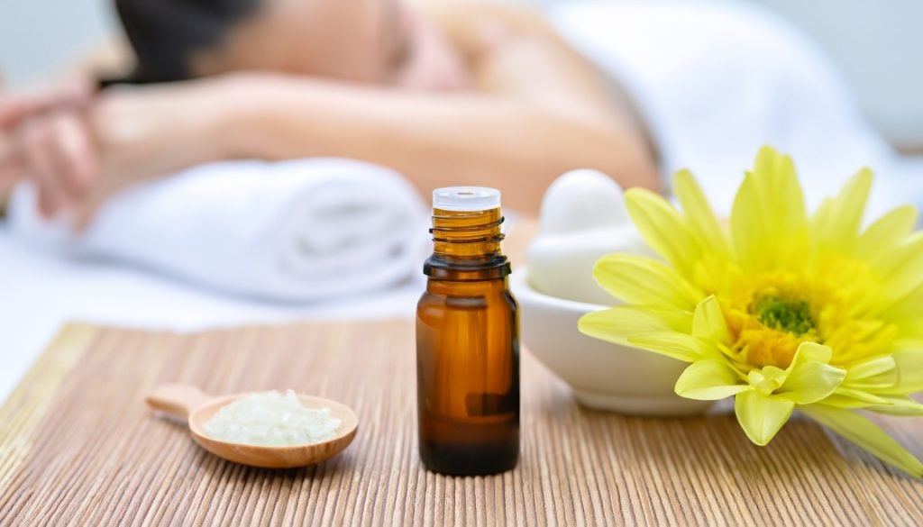 Oleos essenciais colocados ao lado de uma pessoa a receber massagem aromaterapeutica