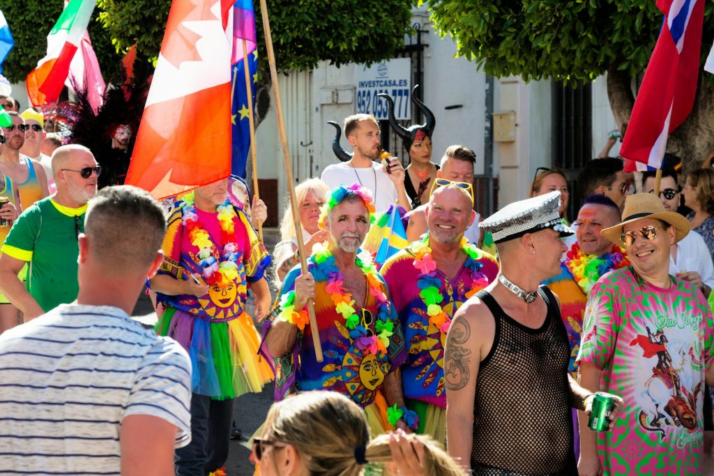 Um grupo de pessoas com trajes e acessórios coloridos participa numa parada vibrante, segurando várias bandeiras e sorrindo, lembrando os festivos Festivais LGBTI em Portugal. Um grupo de pessoas com trajes e acessórios coloridos participa numa parada vibrante, segurando várias bandeiras e sorrindo, lembrando os festivos Festivais LGBTI em Portugal.