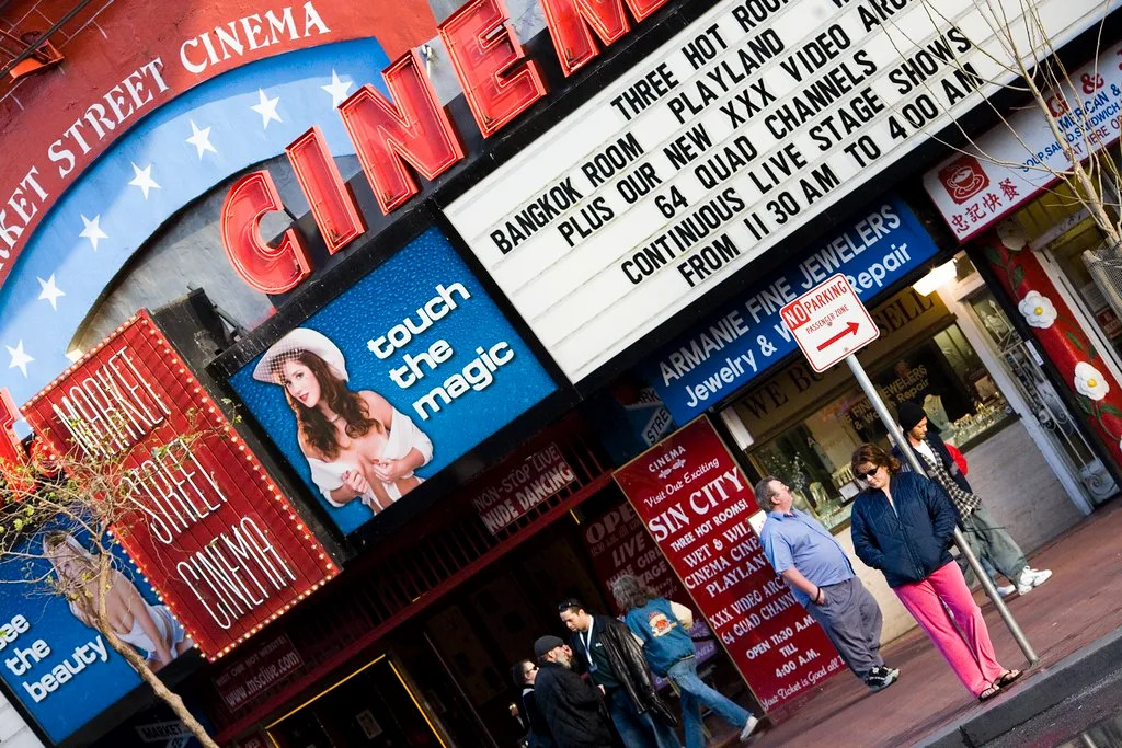 Exterior de um cinema com um letreiro a anunciar vários filmes. Pessoas passam no passeio.