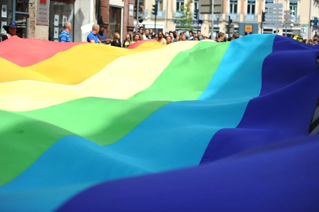 Uma grande bandeira arco-íris LGBTI é transportada por um grupo de pessoas durante um desfile Parada GAY numa rua da cidade.