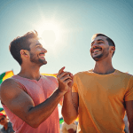 Um casal sorridente de mãos dadas em um ambiente ensolarado, cercado por elementos coloridos da comunidade LGBTQIA+, como bandeiras e grafites vibr...