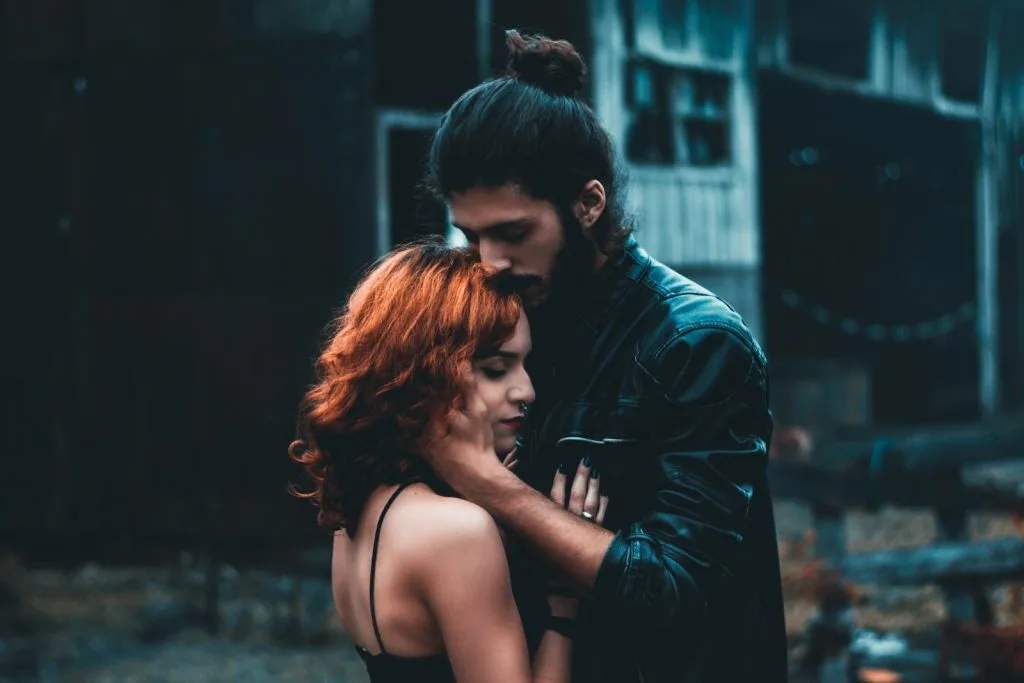 Em frente a um edifício rústico, um homem de cabelos compridos abraça ternamente a sua companheira, a sua ligação tão profunda quanto a orientação de uma terapeuta sexual na relação de casal.