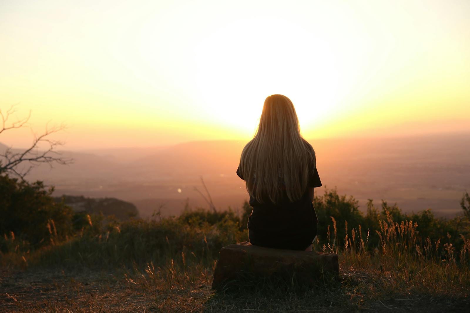 Uma pessoa com cabelo comprido senta-se numa rocha virada para um pôr do sol, abraçando um momento de tranquilidade. A paisagem de colinas e campos desenrola-se como uma tela, simbolizando uma jornada em direção à saúde mental dentro da comunidade LGBT. Uma pessoa com cabelo comprido senta-se numa rocha virada para um pôr do sol, abraçando um momento de tranquilidade. A paisagem de colinas e campos desenrola-se como uma tela, simbolizando uma jornada em direção à saúde mental dentro da comunidade LGBT.
