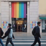 Pessoas passam diante de um edifício que ostenta uma grande bandeira arco-íris do orgulho e um letreiro "LGBTI" sobre a entrada; cartazes nas paredes promovem Apoio Psicológico LGBTI em Lisboa – Encontre Ajuda.
