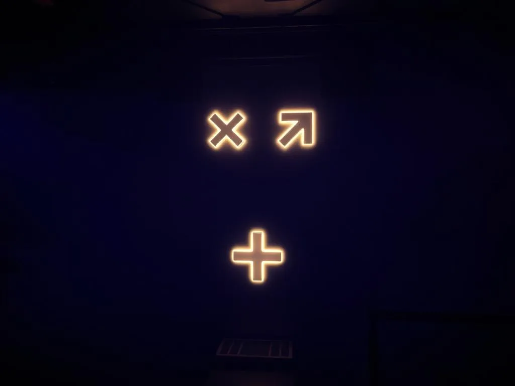 Os ícones estão em uma parede escura: um "X", uma seta para cima e direita, e um sinal de mais, evocando uma linguagem inclusiva.