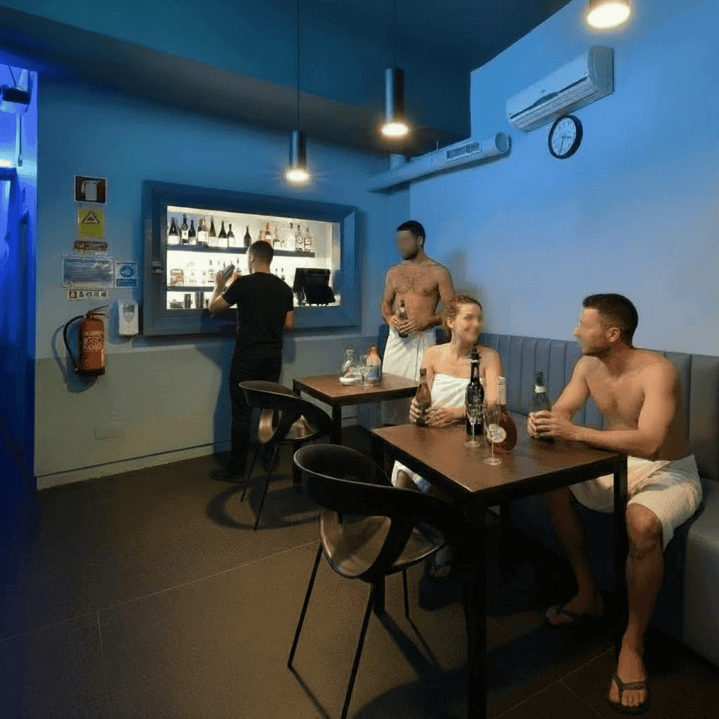 Na SaunApolo 56, três pessoas de toalha conversam sentadas nas mesas na zona do bar. Funcionário na zona do balcão. (fotos anonimizadas e com autorização)