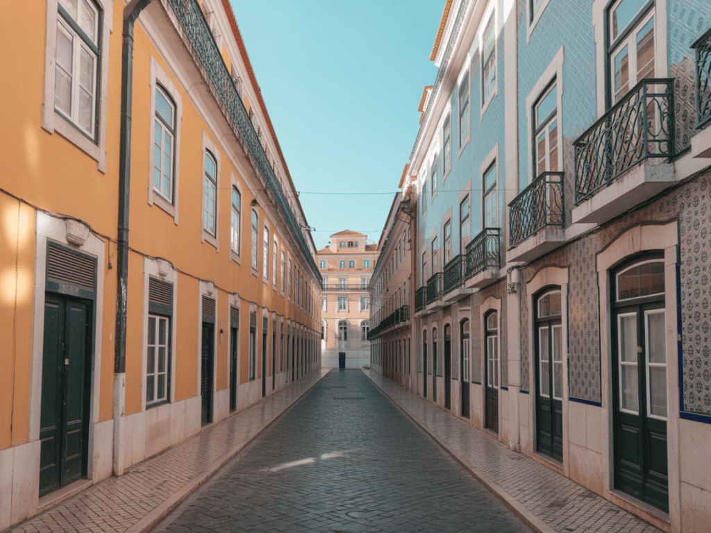 Rua estreita de calçada, ladeada de edifícios amarelos e azuis com varandas e portadas, sob céu limpo-ideal nos primeiros passos em Lisboa após a migração LGBTQ+. Rua estreita de calçada, ladeada de edifícios amarelos e azuis com varandas e portadas, sob céu limpo-ideal nos primeiros passos em Lisboa após a migração LGBTQ+.